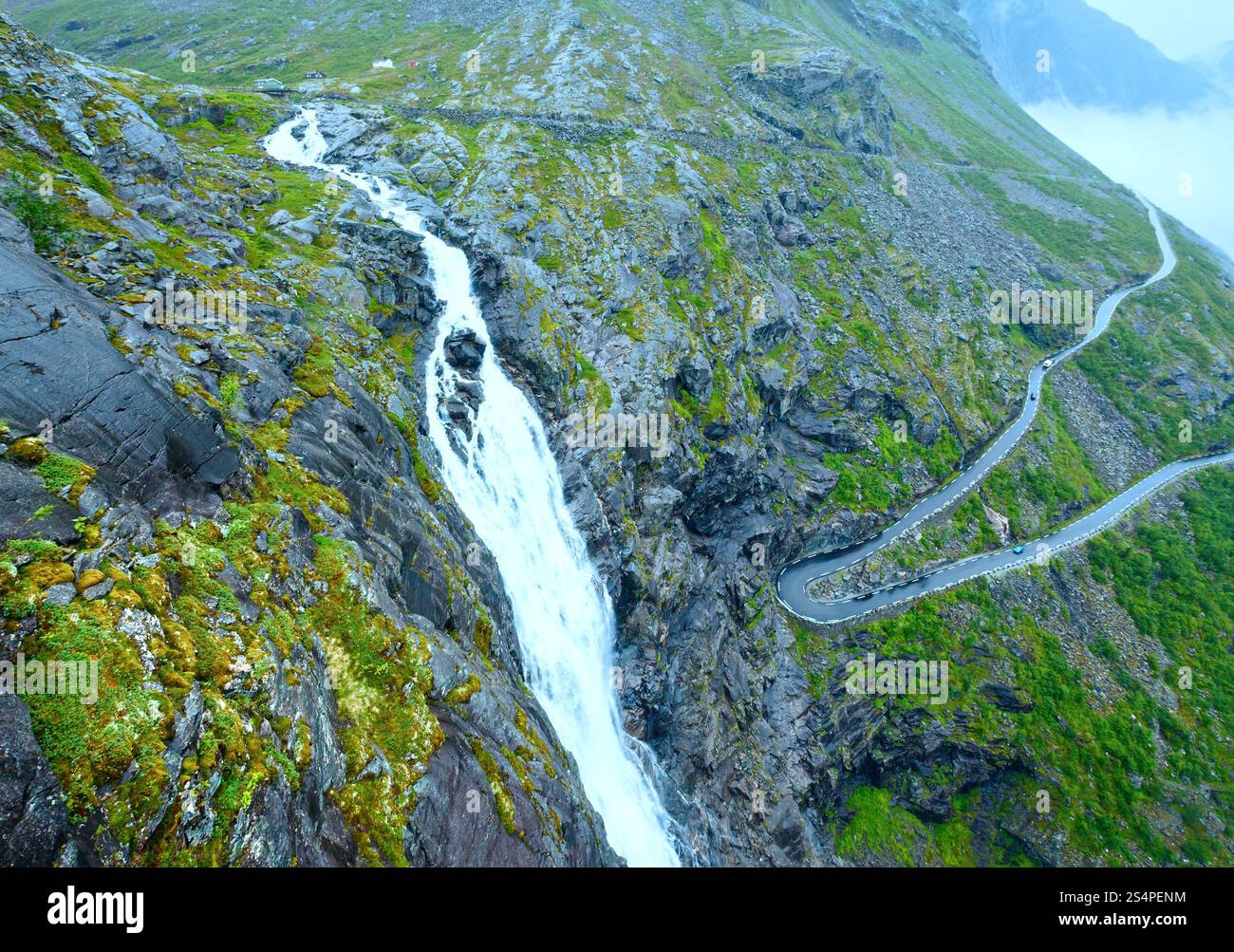 Summer mountain cloudy view with waterfall and serpentine road on slope (Norway). Stock Photo