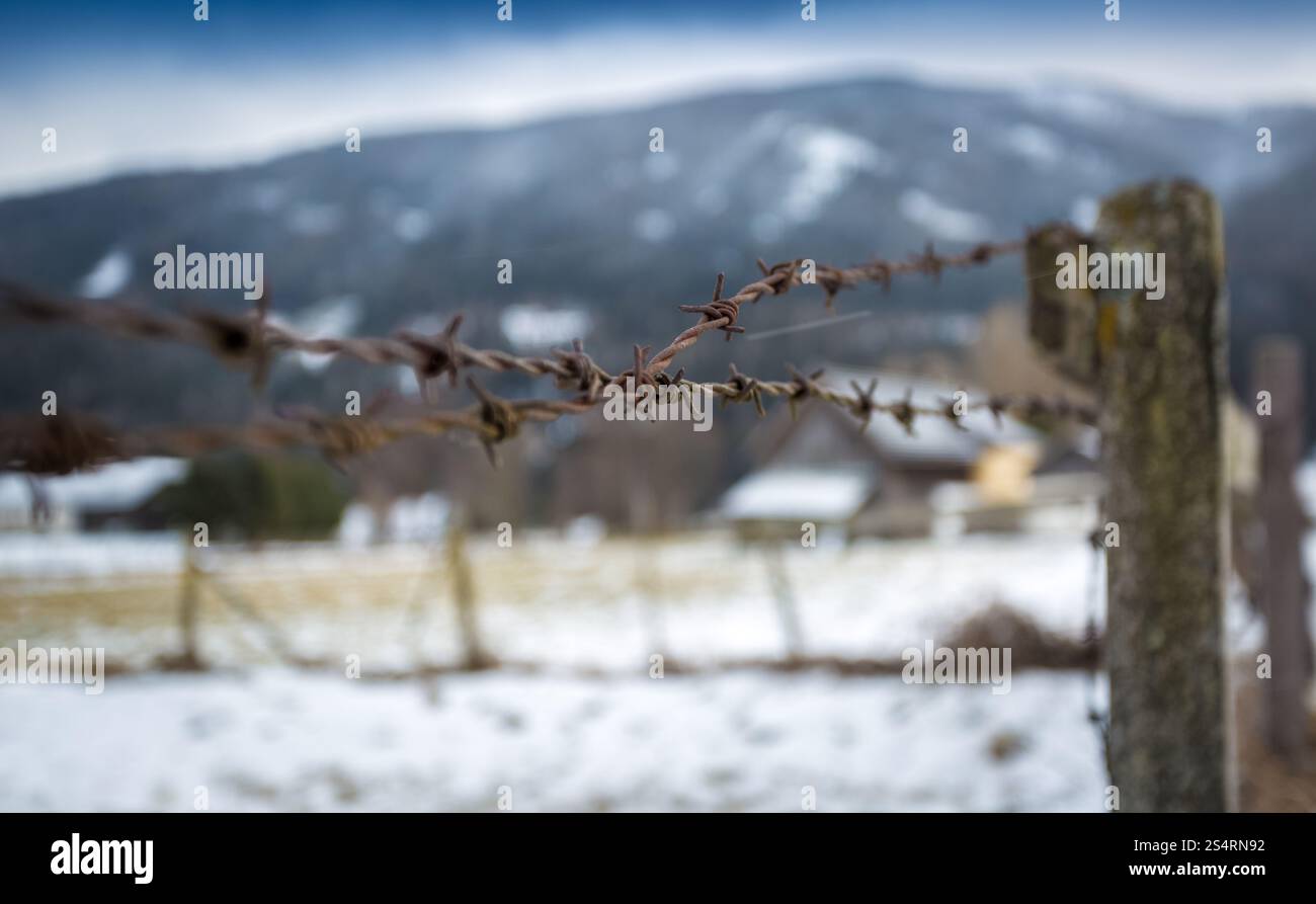 Closeup photo of barbed wire on wooden fence on field covered in snow Stock Photo