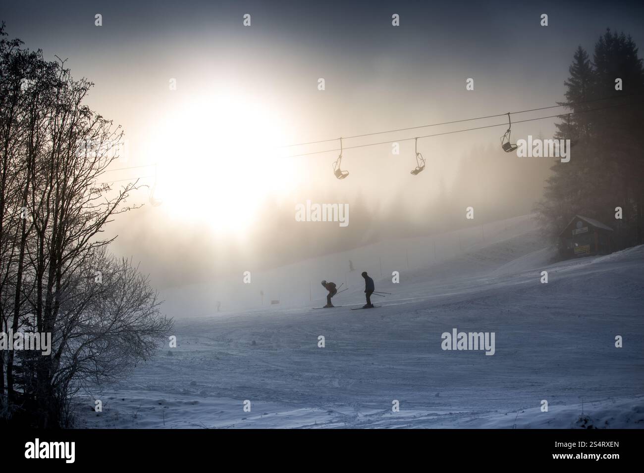 Beautiful silhouette photo of riding skiers and ski lift against bright winter sun Stock Photo