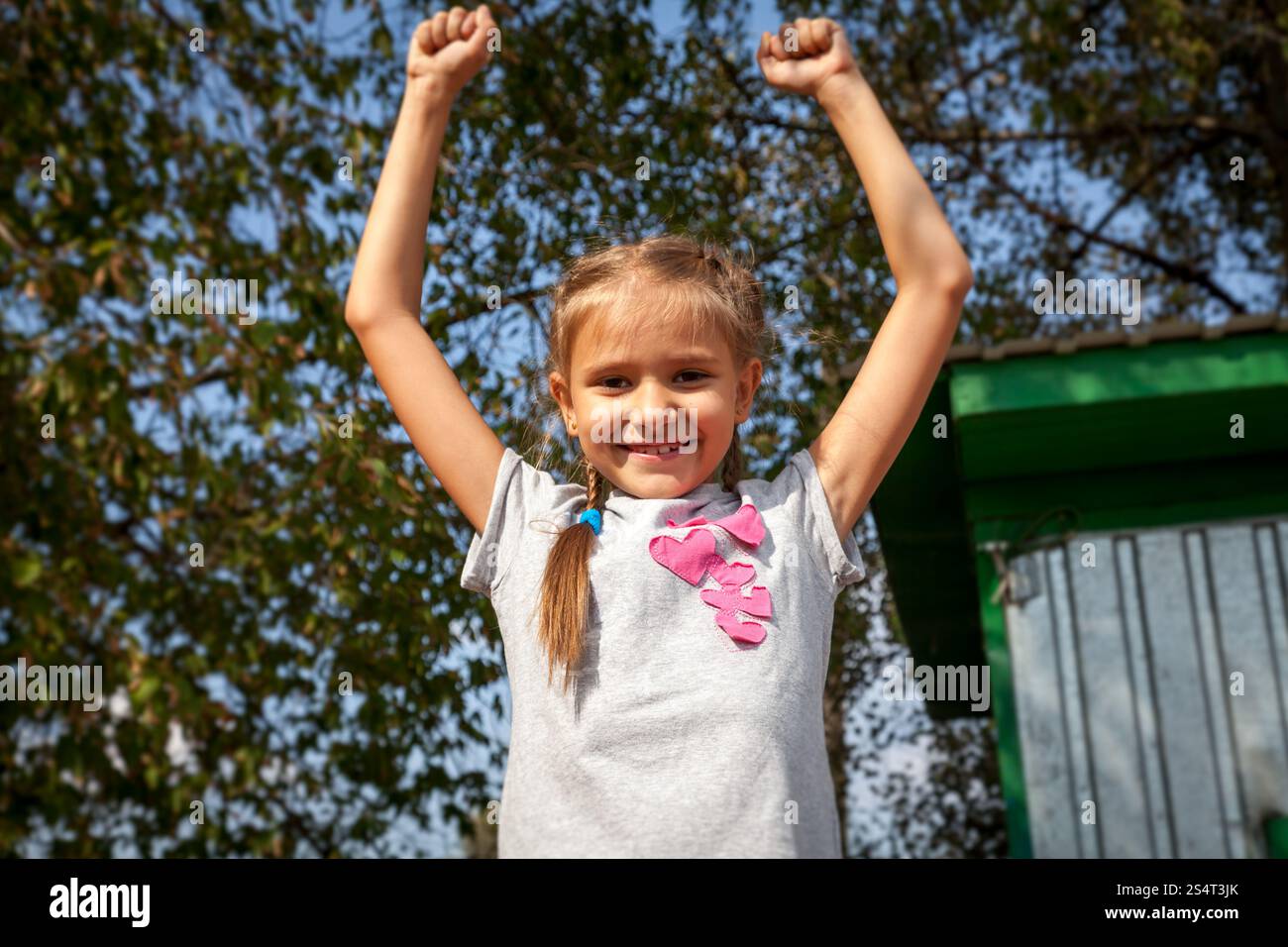 Portrait of happy little girl holding hands up at park at sunny day ...