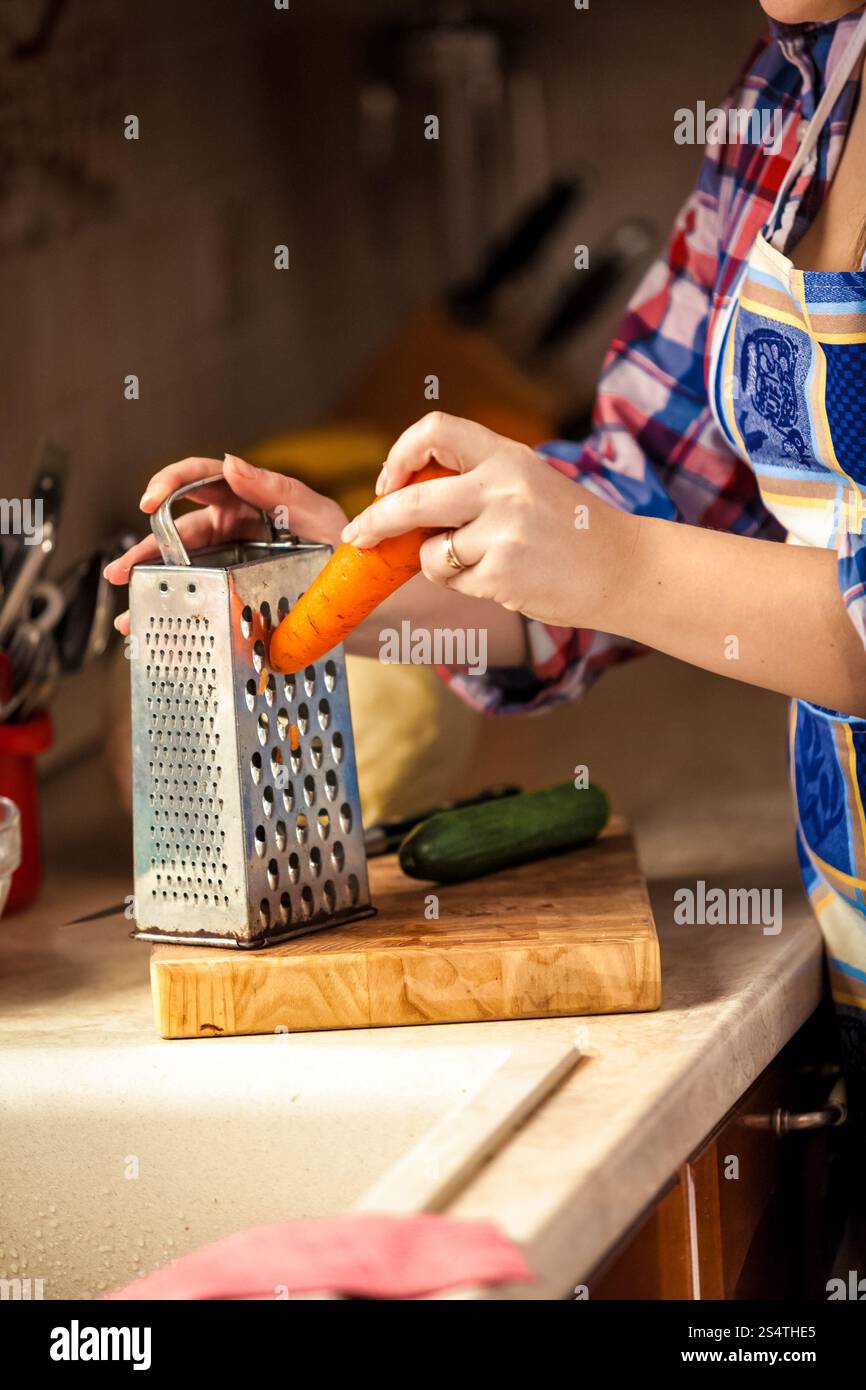 Closeup photo of woman grating carrot on wooden board Stock Photo
