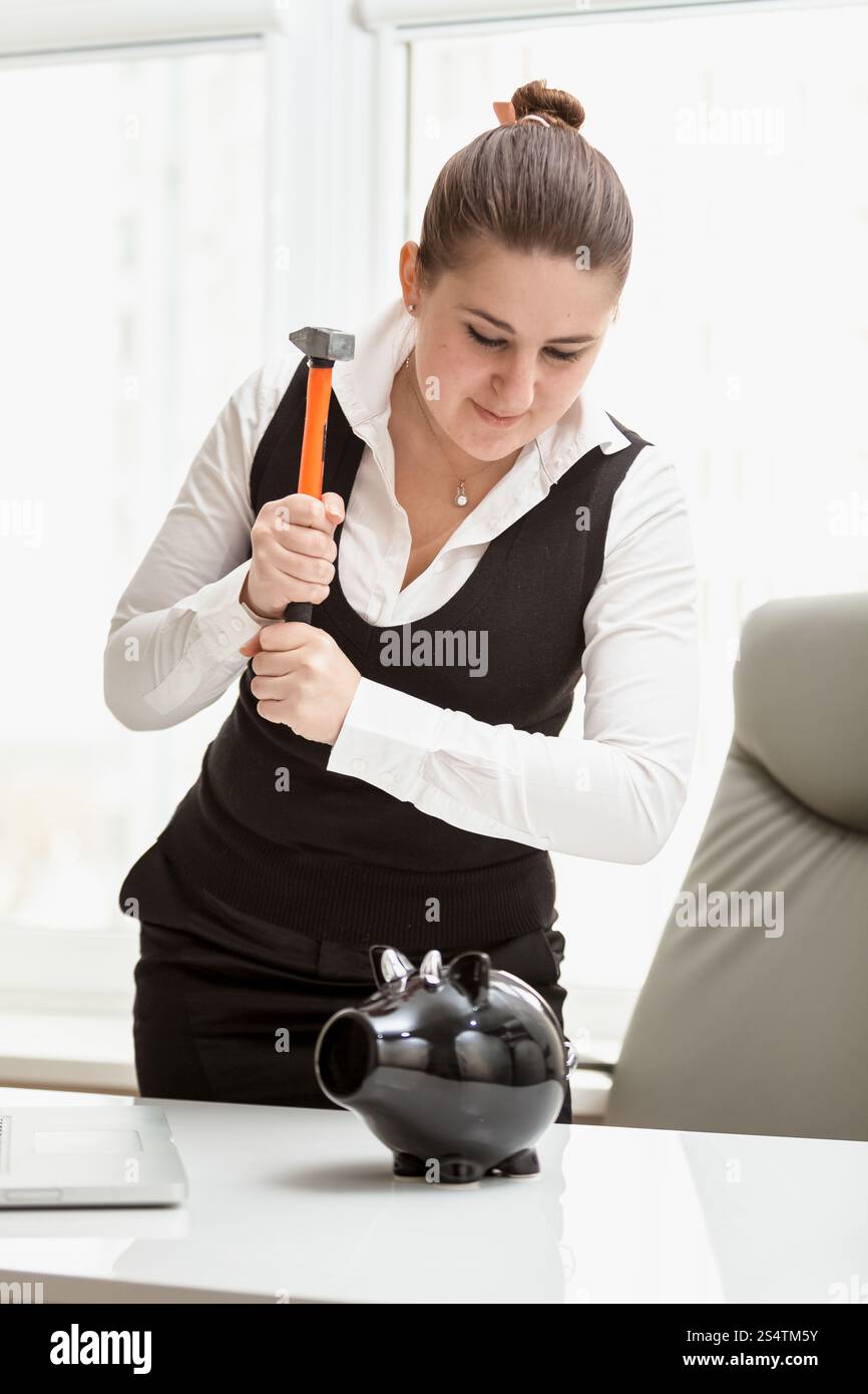 Closeup portrait of brunette businesswoman trying to break piggy bank Stock Photo