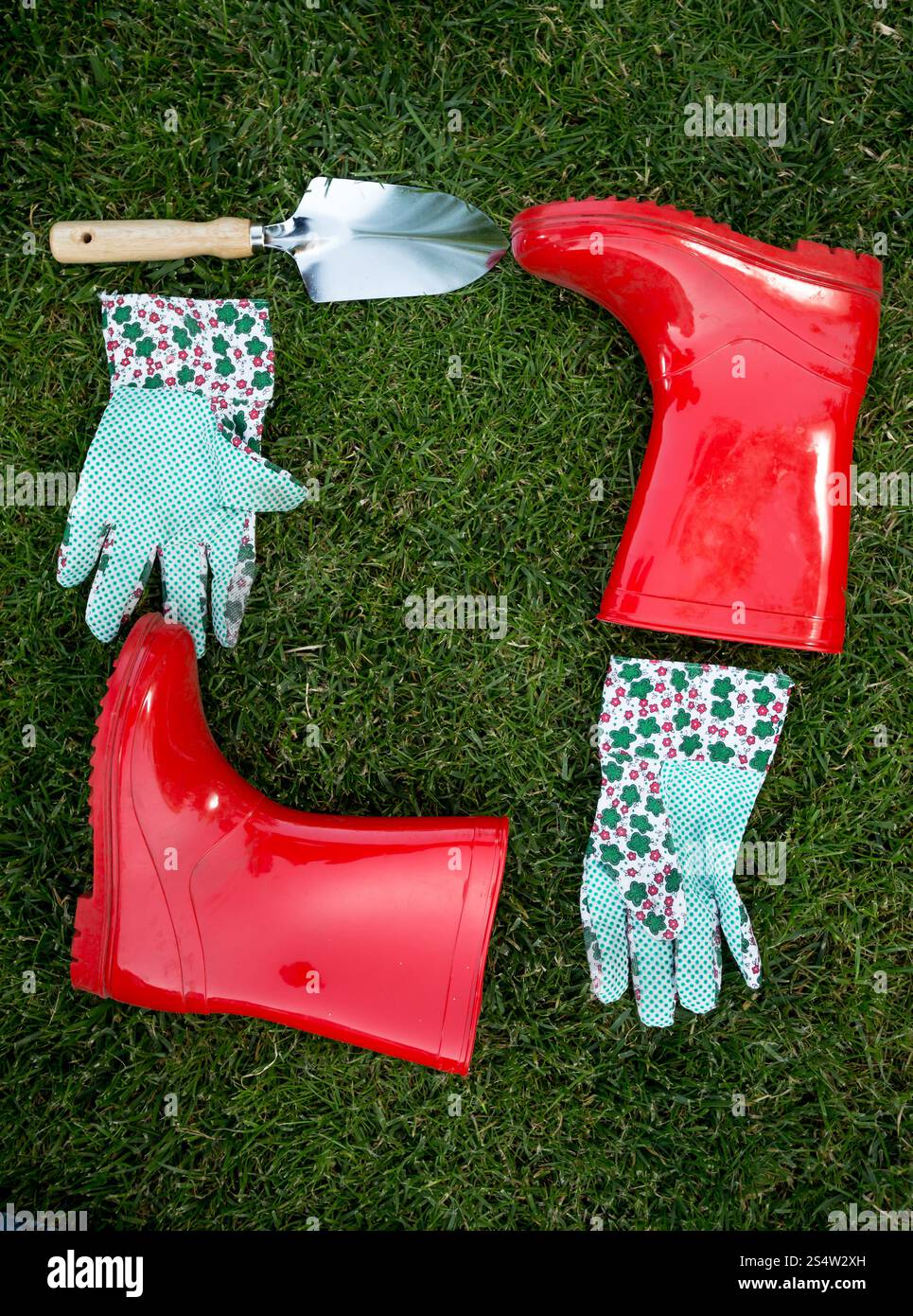 Closeup photo of garden gloves, spade and red rubber boots lying on green grass Stock Photo