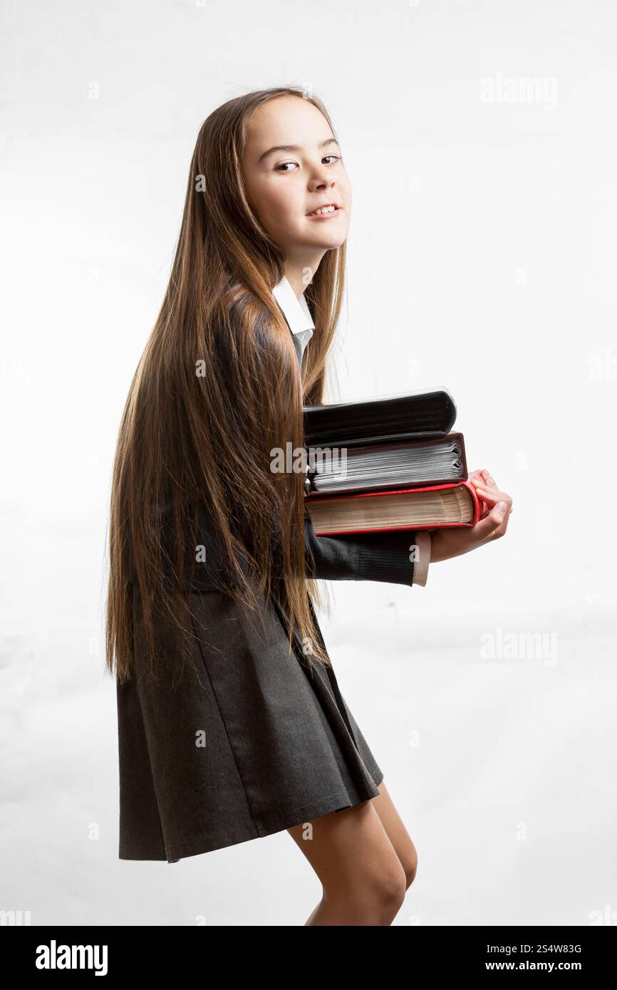 Little schoolgirl in uniform carrying heavy stack of books Stock Photo ...