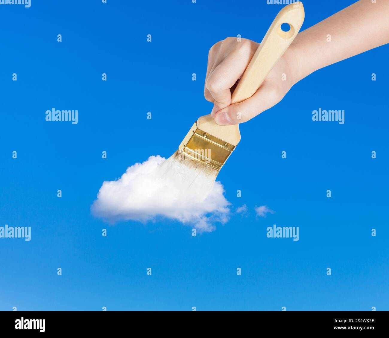 weather concept - hand with paintbrush paints lonely white little cloud in the summer blue sky Stock Photo