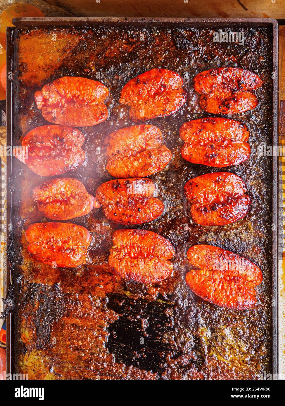 Close-up of sizzling chorizo sausages grilling on a hot, seasoned metal plate. Stock Photo