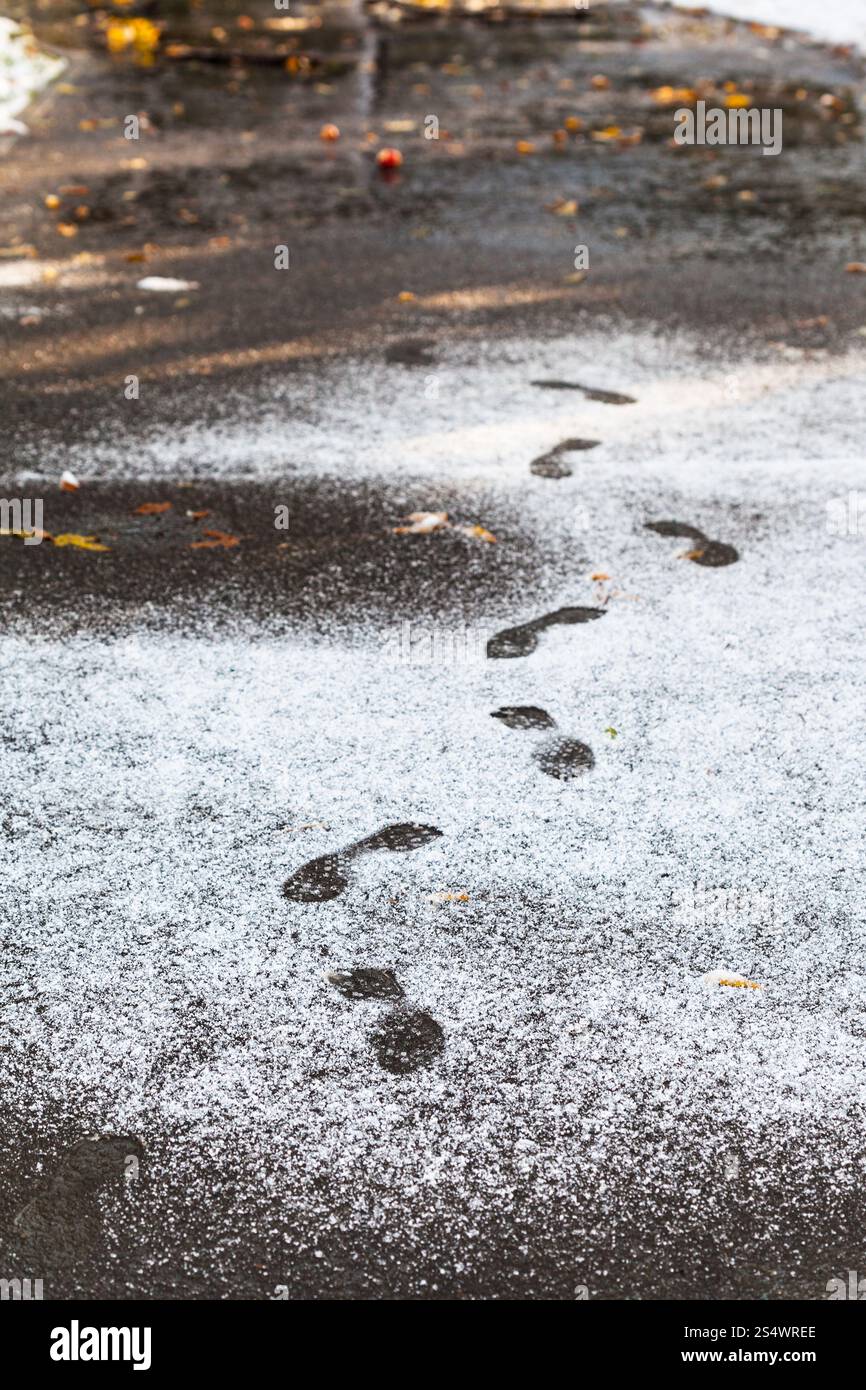 footprints in wet path in city park covered by first snow in autumn Stock Photo