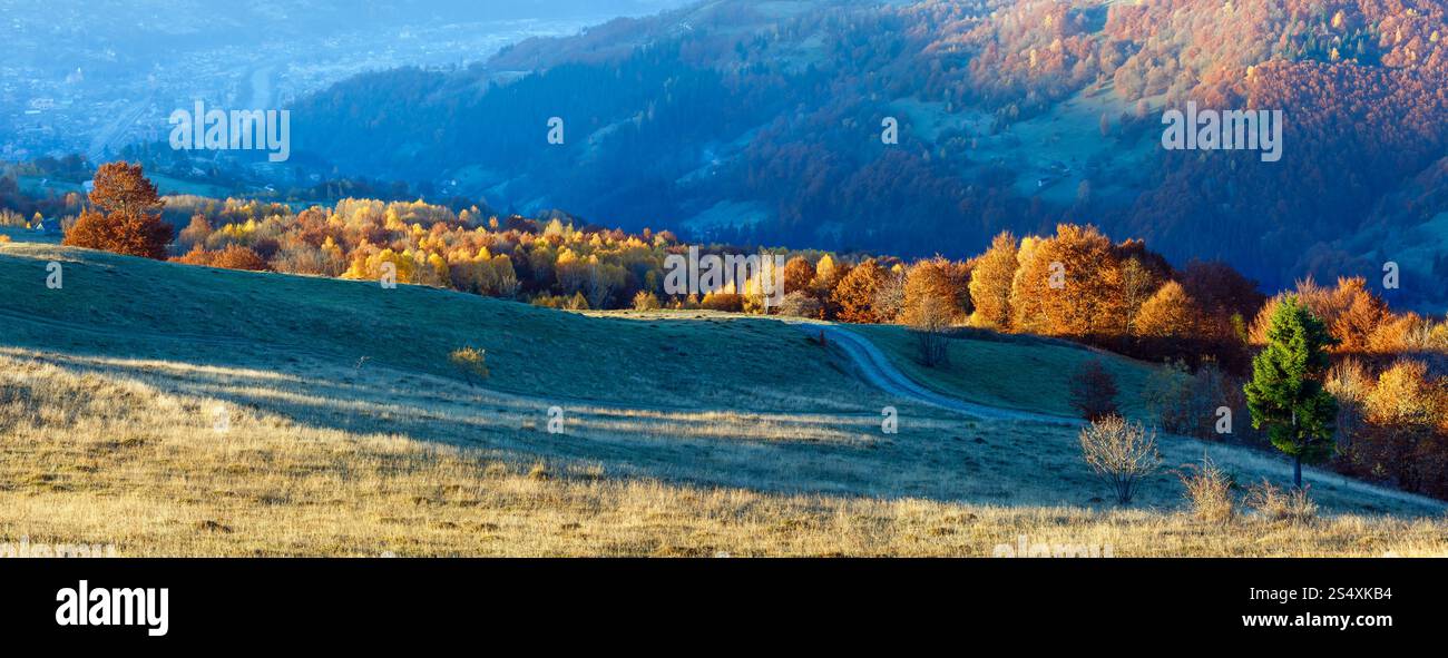 Rural road on autumn misty mountain slope and village in valley ...