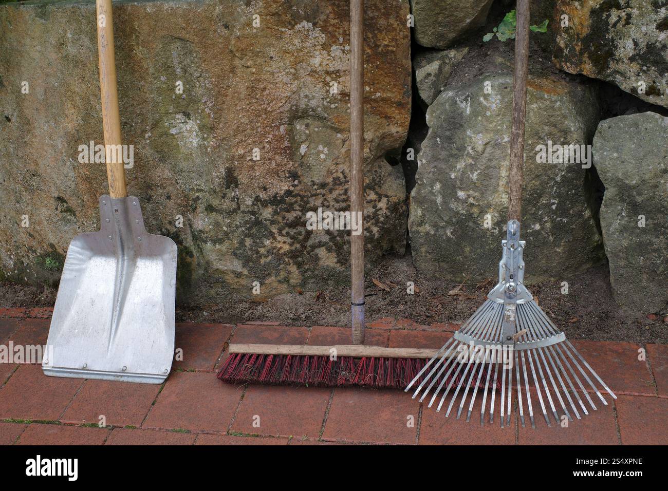 Garden tools standing against an old wall. These are tools to collect leaves: shovel, broom and leaf rake Stock Photo