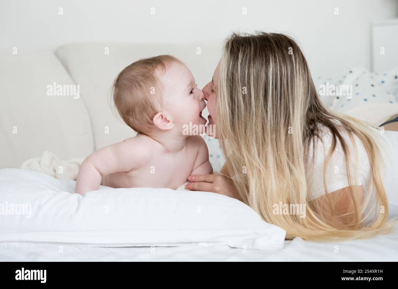 Closeup portrait of cheerful baby with mother lying on big white pillow Stock Photo
