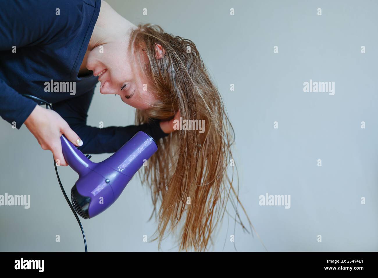 Young woman drying her hair with a hairdryer isolated on studio ...
