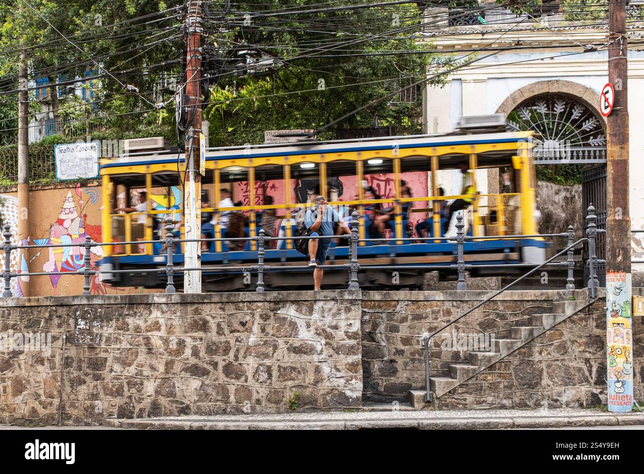 A Man talks on his phone as a Tram full of people passes behind him, Santa Teresa, Brazil. Stock Photo