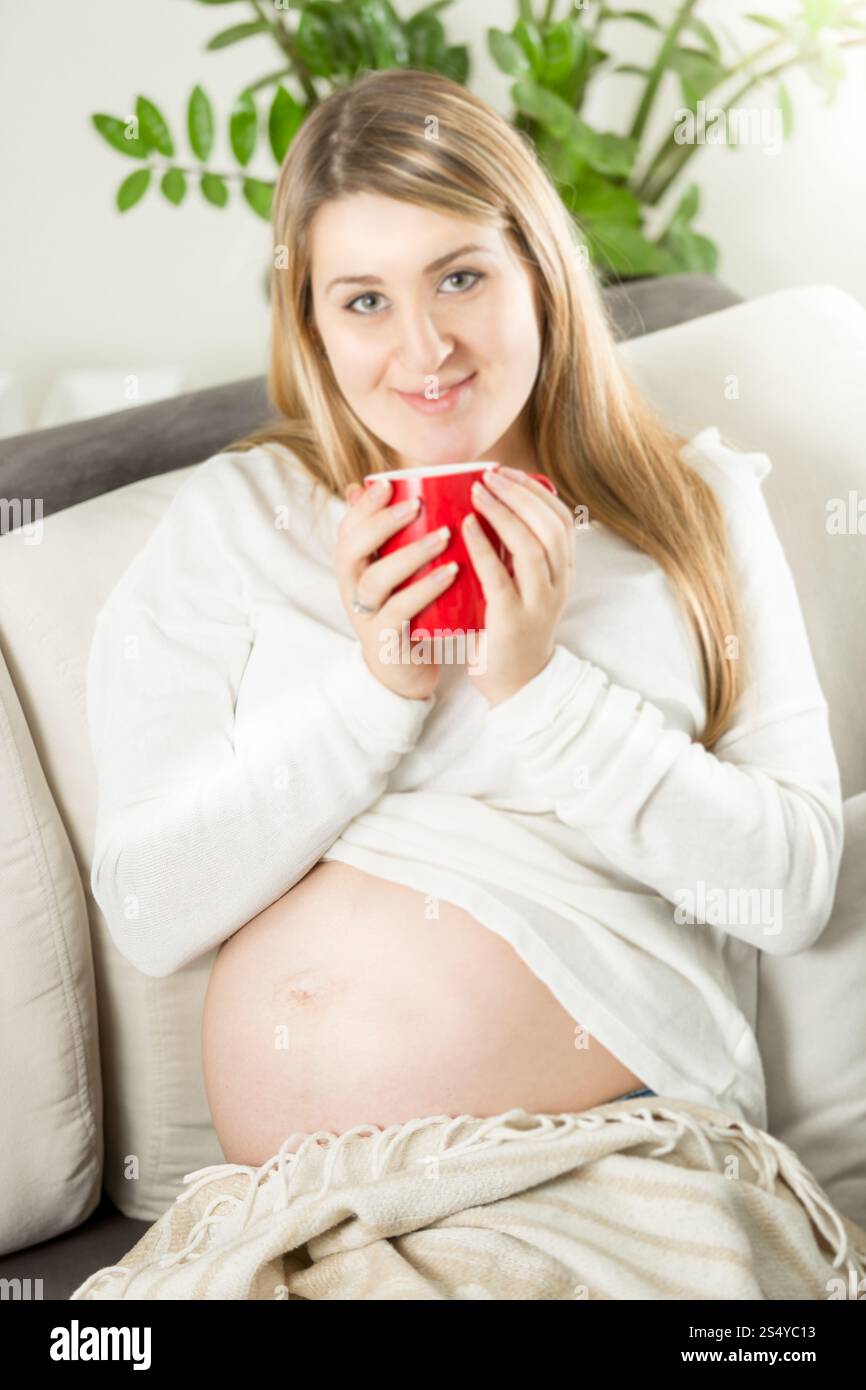 Beautiful smiling pregnant woman relaxing on sofa with cup of tea Stock ...