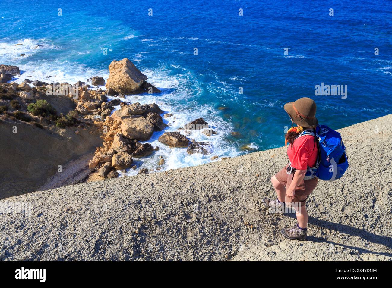 Hiker on cliff edge looing at coastal rocks, Tal Blata, Malta Stock Photo