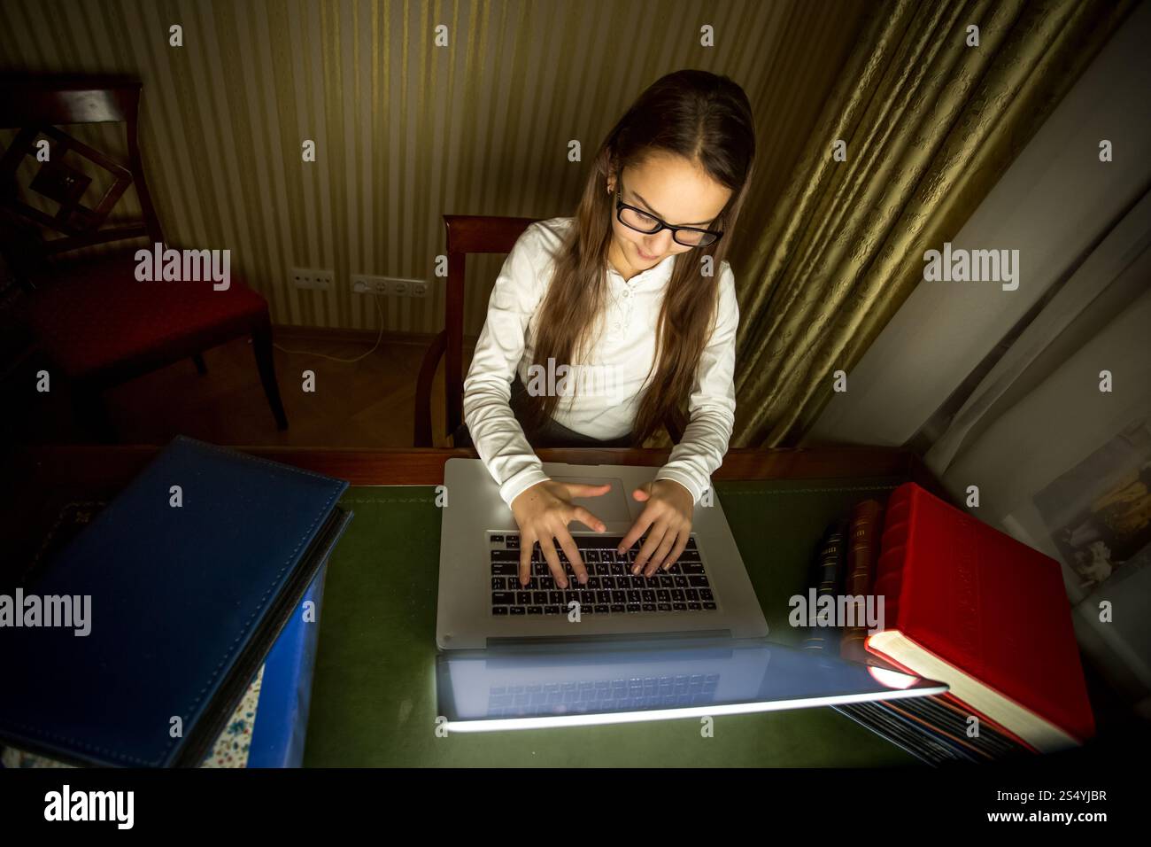 Smiling schoolgirl in eyeglasses working at computer at dark room Stock ...