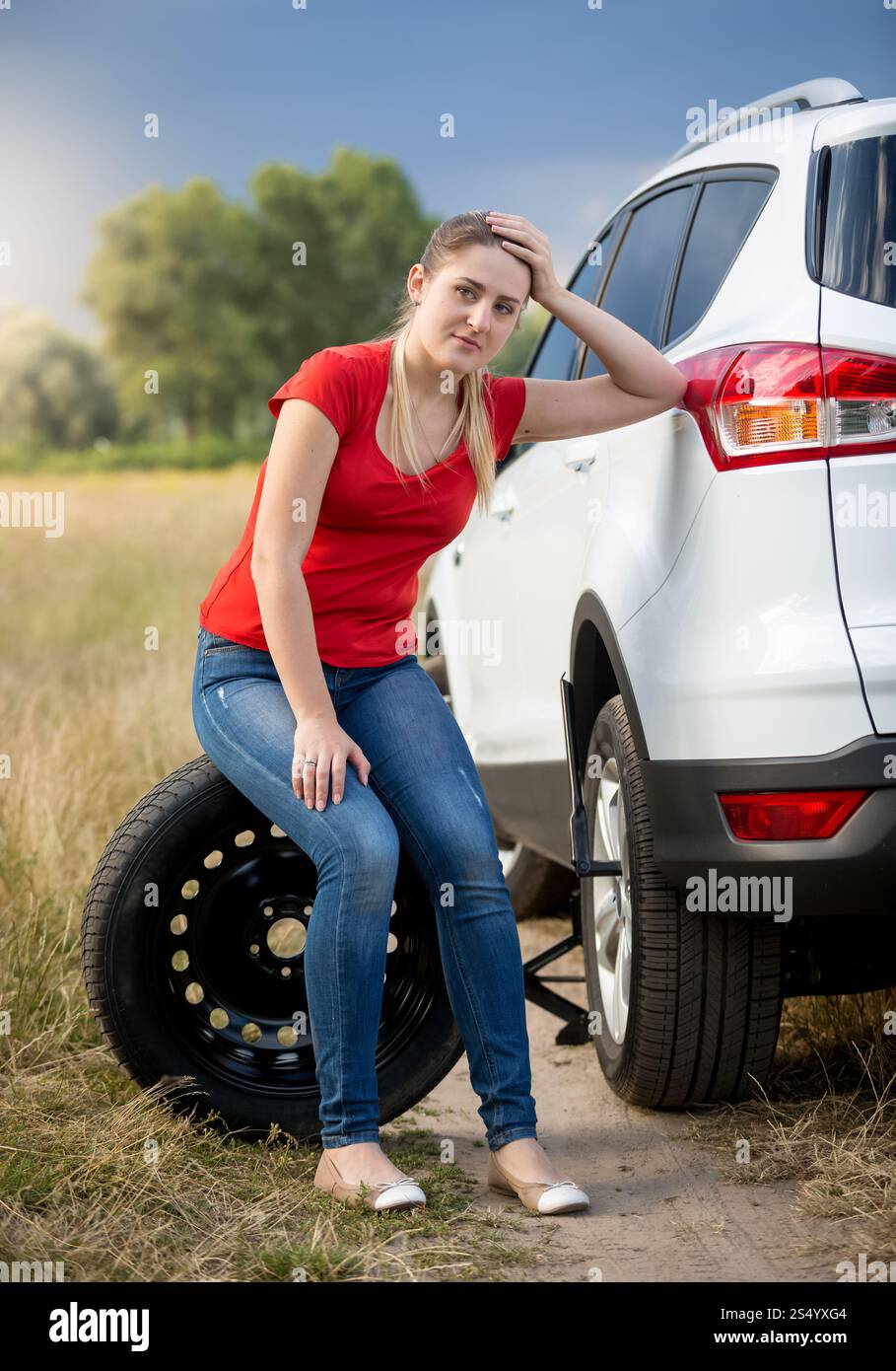 Upset woman sitting next to broken car at field Stock Photo