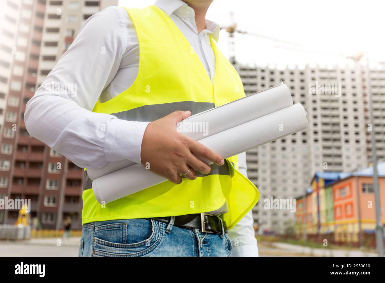 Closeup image of engineer in safety vest holding rolled blueprints Stock Photo