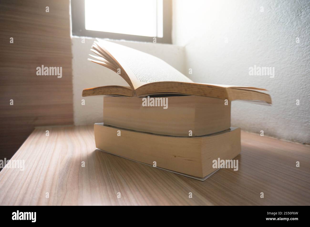 Open old books on a wooden table with window light. Stock Photo