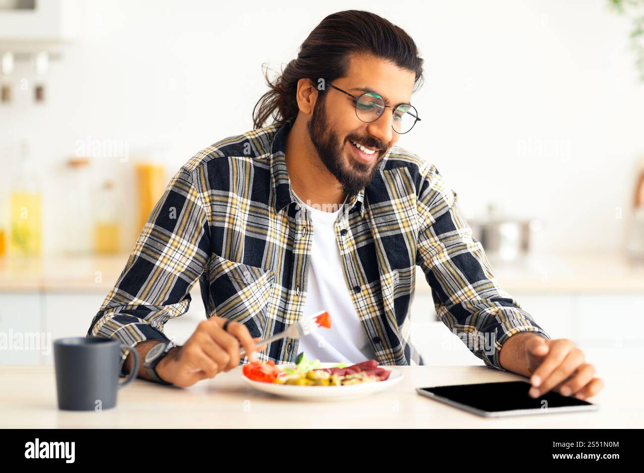 Happy indian guy having lunch and using digital tablet Stock Photo