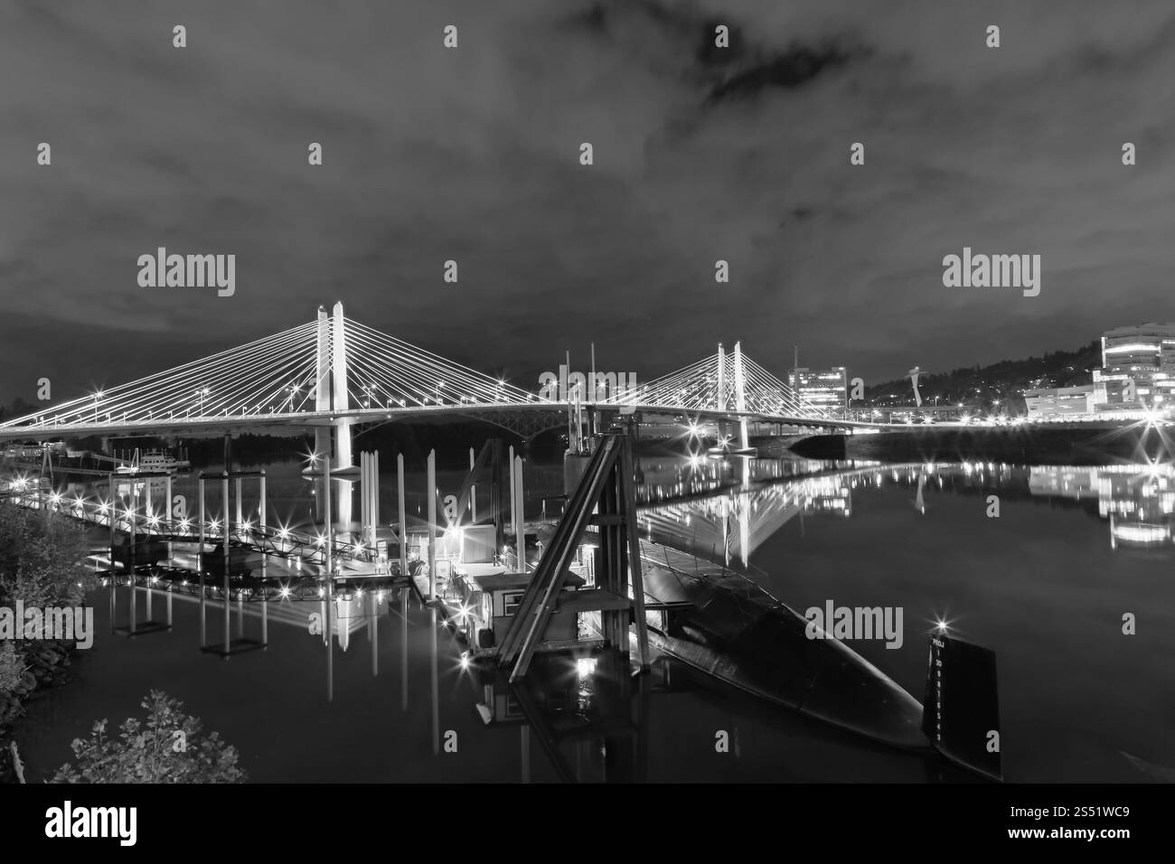 Illuminated Modern Suspension Bridge Over Calm Waters in Black and White Urban Landscape with the USS Blueback Submarine in the Foreground Stock Photo