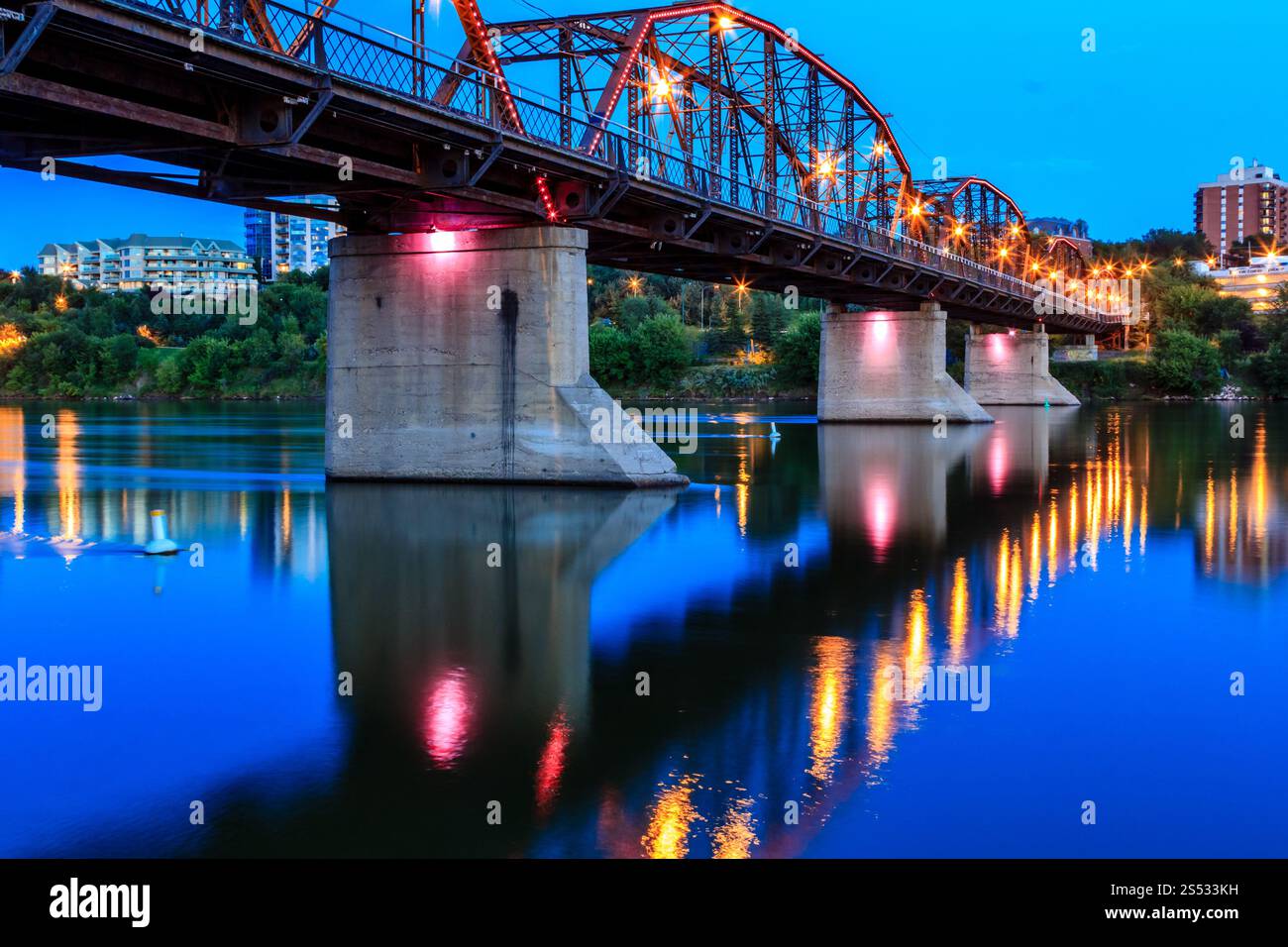A bridge spans a river at night, with lights illuminating the structure. The water is calm and reflective, creating a serene atmosphere Stock Photo