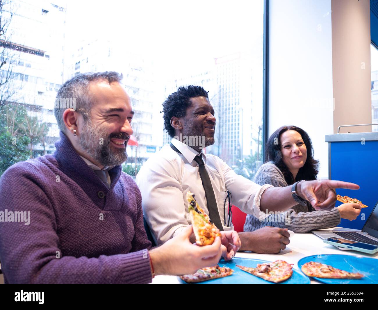 Colleagues Laughing and Pointing While Sharing Pizza Stock Photo