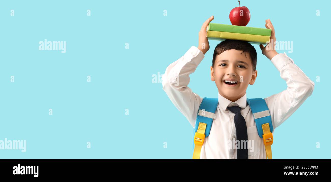 Little schoolboy with backpack, apple and books on light blue ...