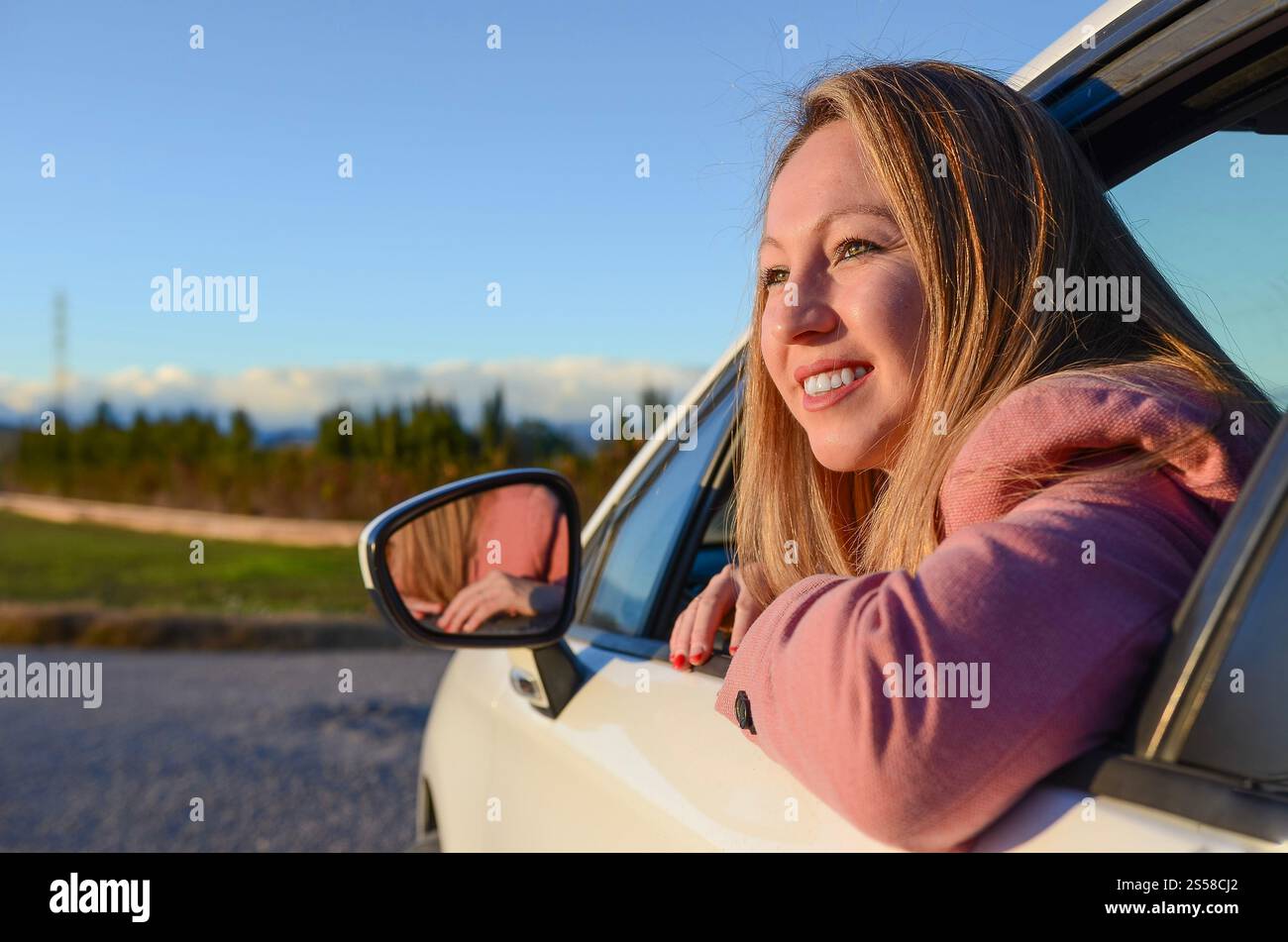 Young woman enjoying road trip leaning out of car window, looking at ...