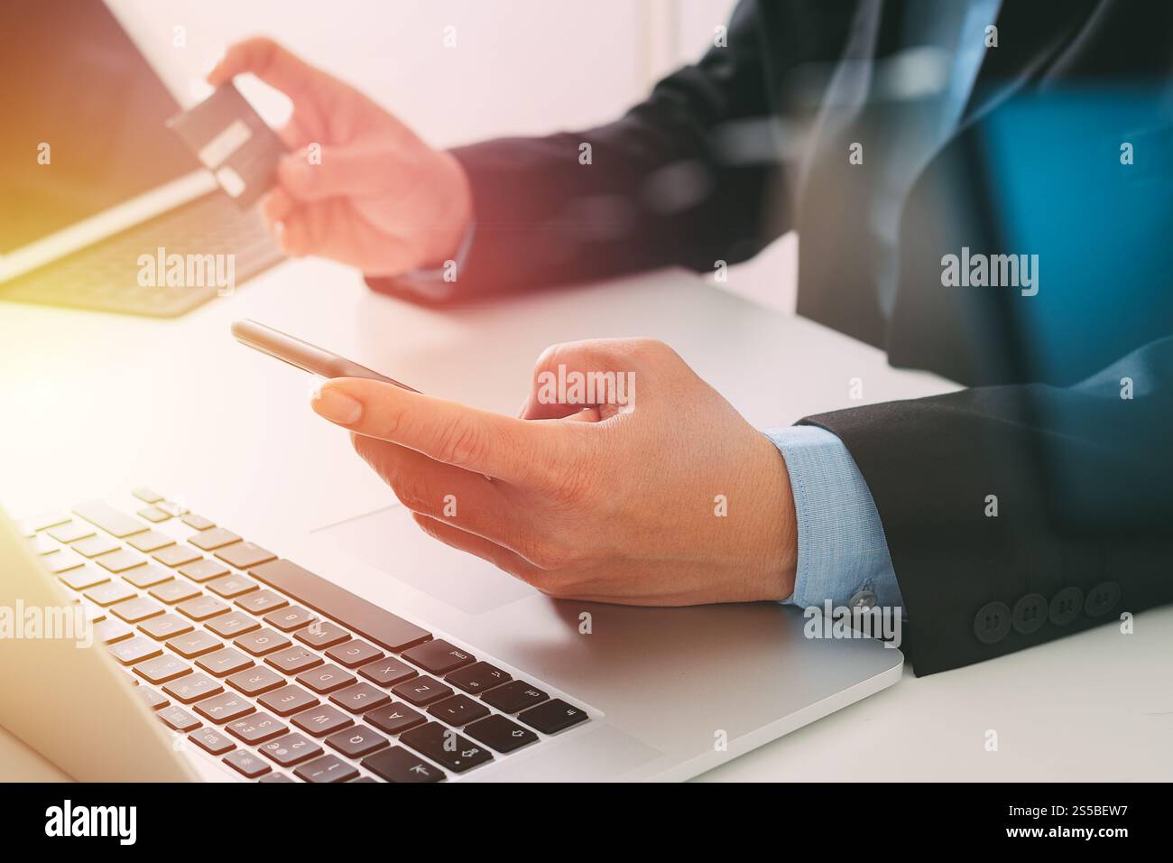 businessman making credit card purchase online with mobile phone and laptop computer on modern desk Stock Photo