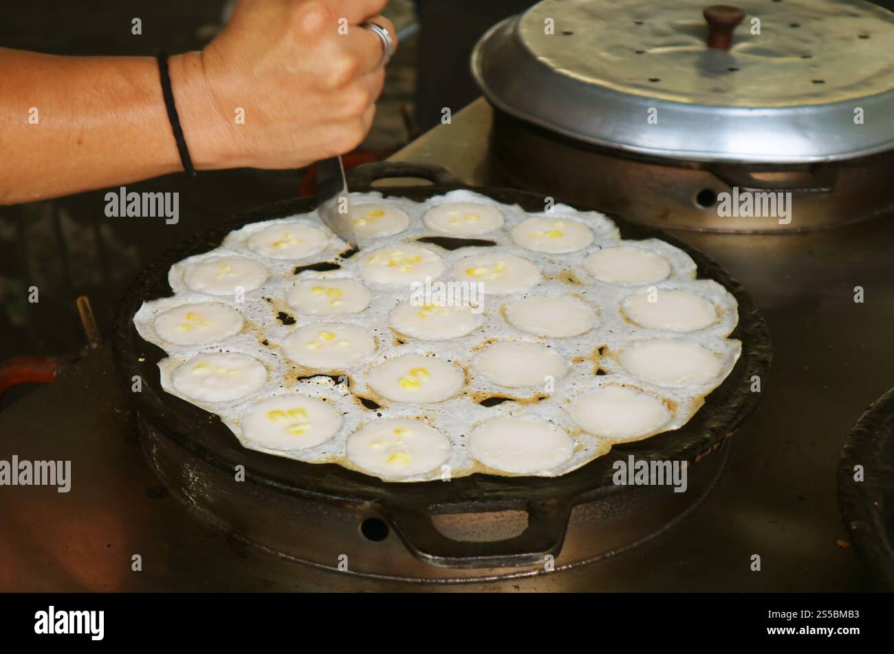 Vendor using tool cutting the edges of nearly done Thai coconut milk pancakes called Kanom krok Stock Photo