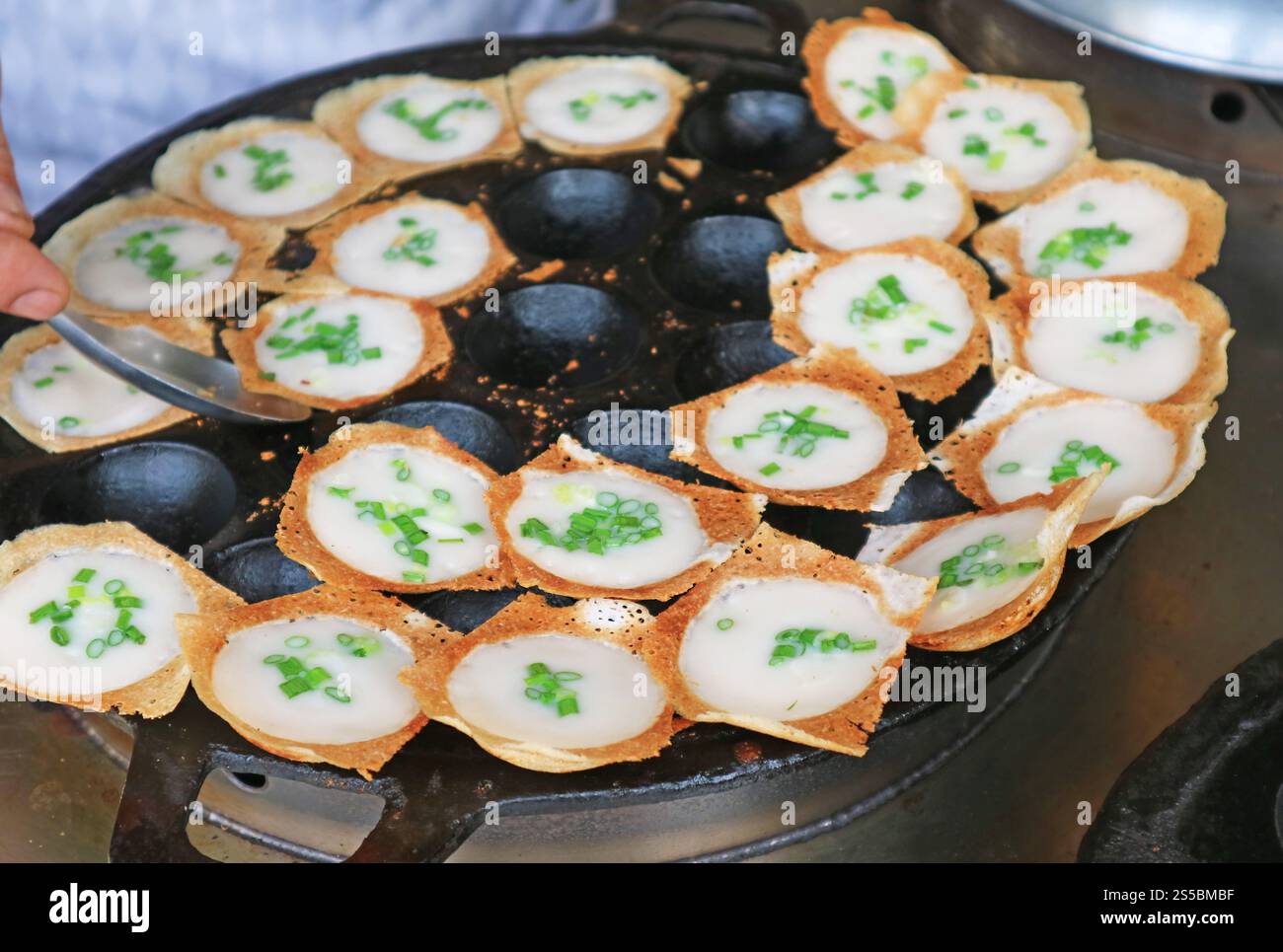 vendor taking Kanom Krok, popular Thai coconut milk pancake out from the pan when ready to serve Stock Photo