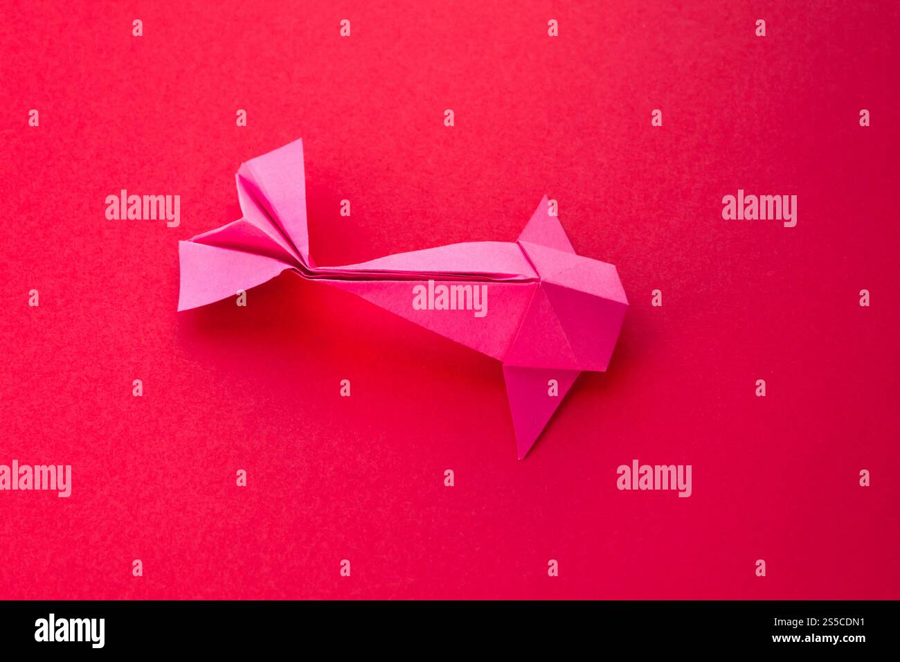 Pink paper fish origami isolated on a blank red background. Pink paper ...