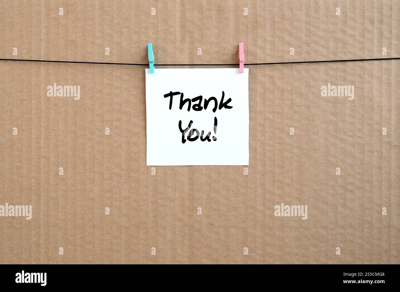 Thank you! Note is written on a white sticker that hangs with a clothespin on a rope on a background of brown cardboard Stock Photo