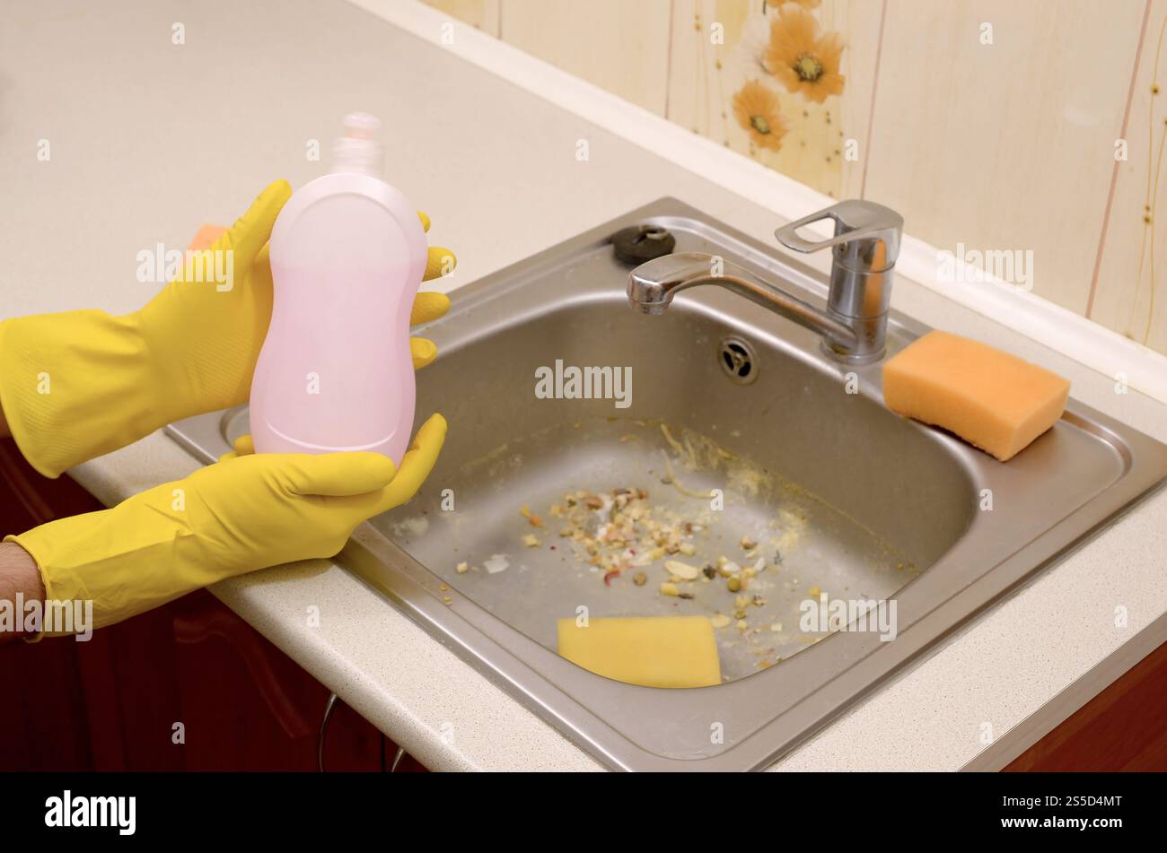 People housework washing-up and housekeeping concept. Cleaner shows liquid cleanser detergent bottle at dirty kitchen sink with food particles before Stock Photo