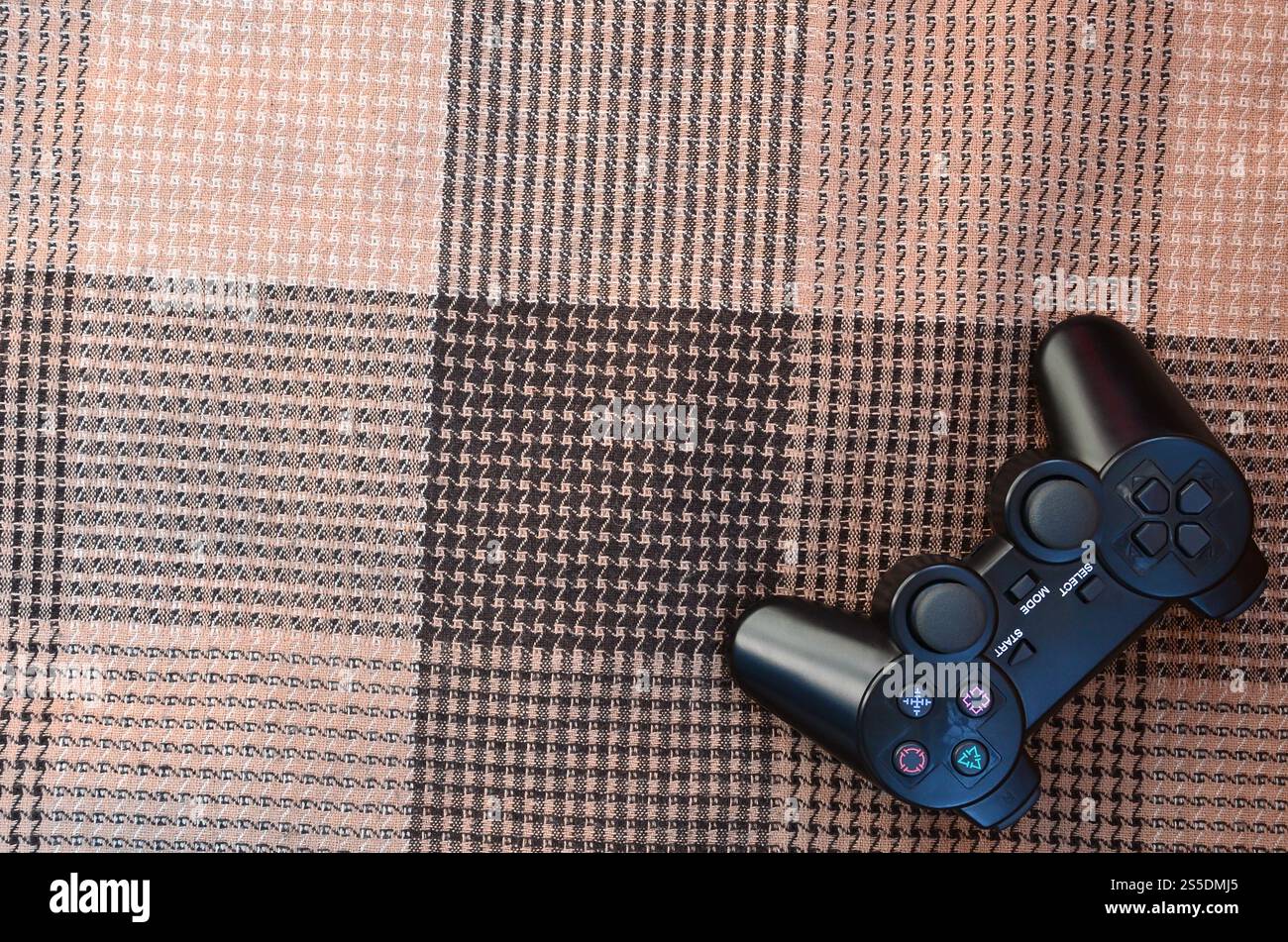 The video game controller from the game console is on the checkered sofa. Wireless device for controlling during video games. Video game controller Stock Photo