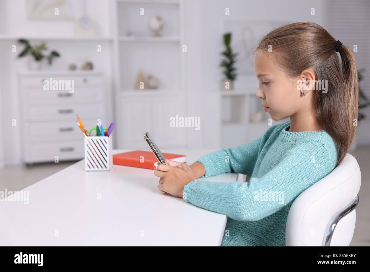 Girl with correct posture using smartphone at white desk indoors Stock ...