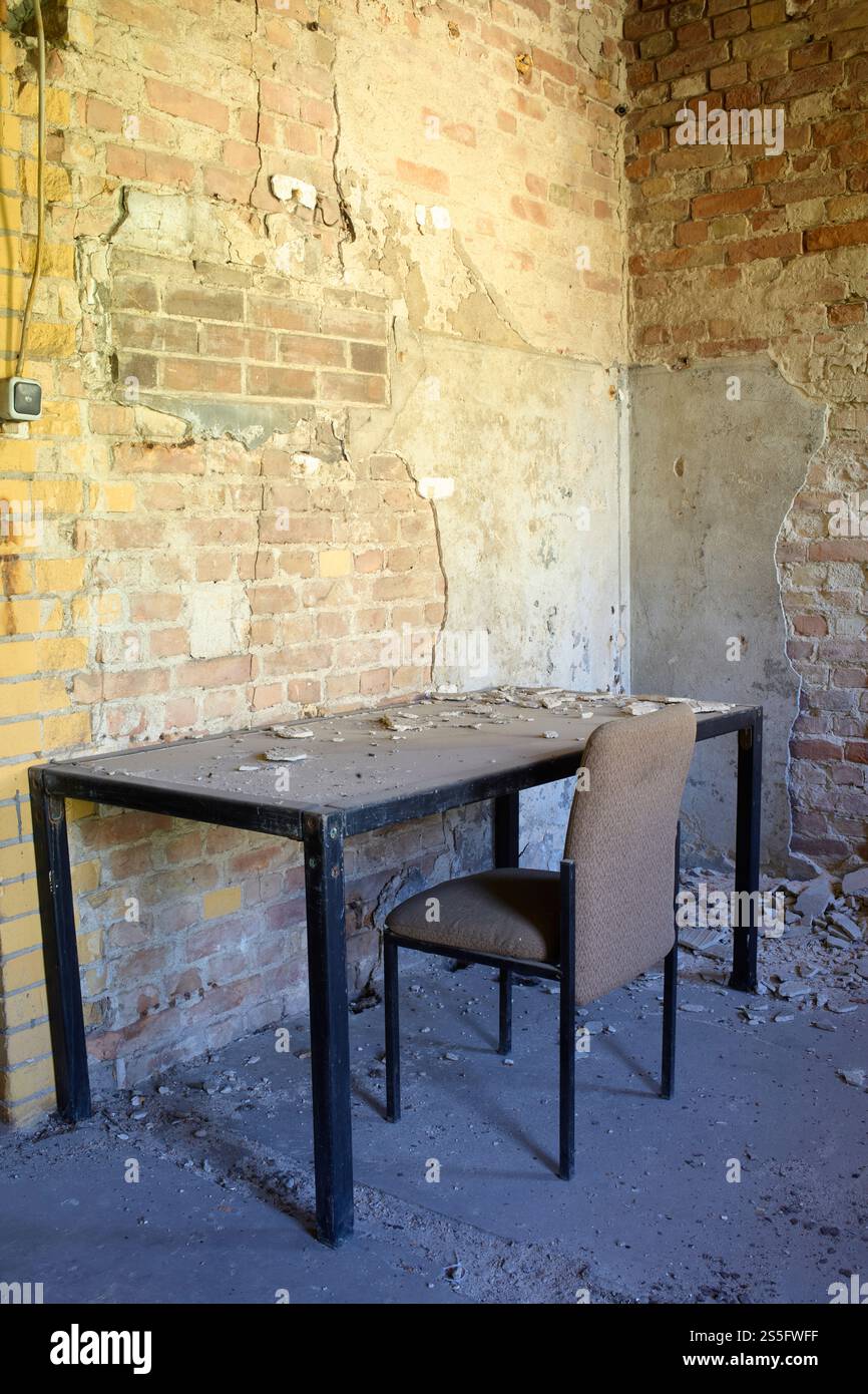 An abandoned office with a worn-out table and chair against a partially destroyed brick wall, Berlin, Germany Stock Photo