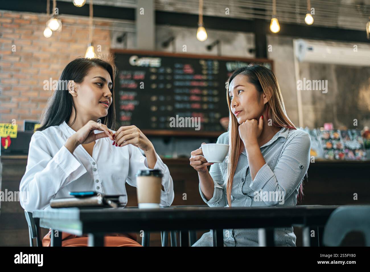 Two women sitting and drinking coffee and chatting in a cafe Stock Photo