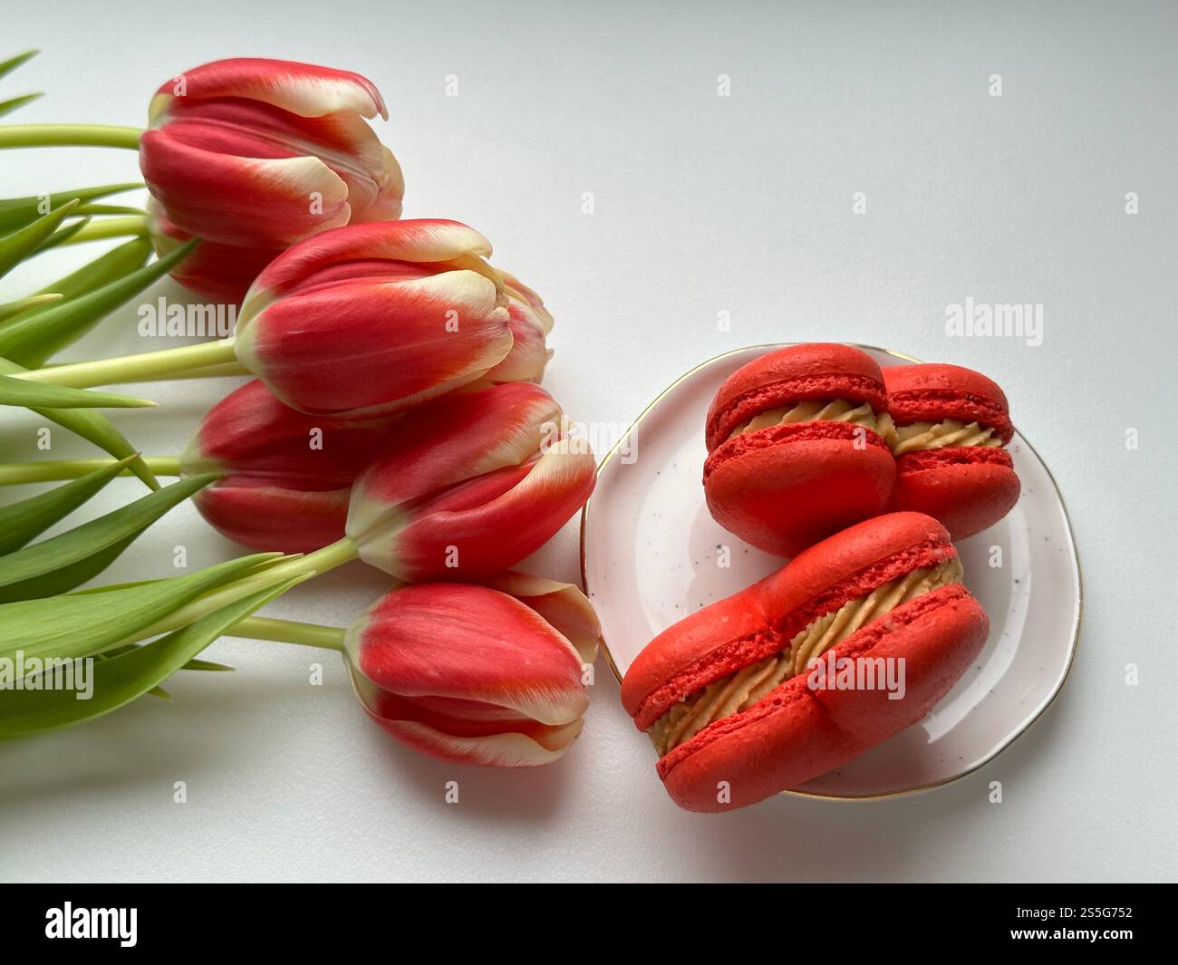 French dessert red hearts macarons on the white plate and red tulips on the white background - Smartphone Captured Stock Image
