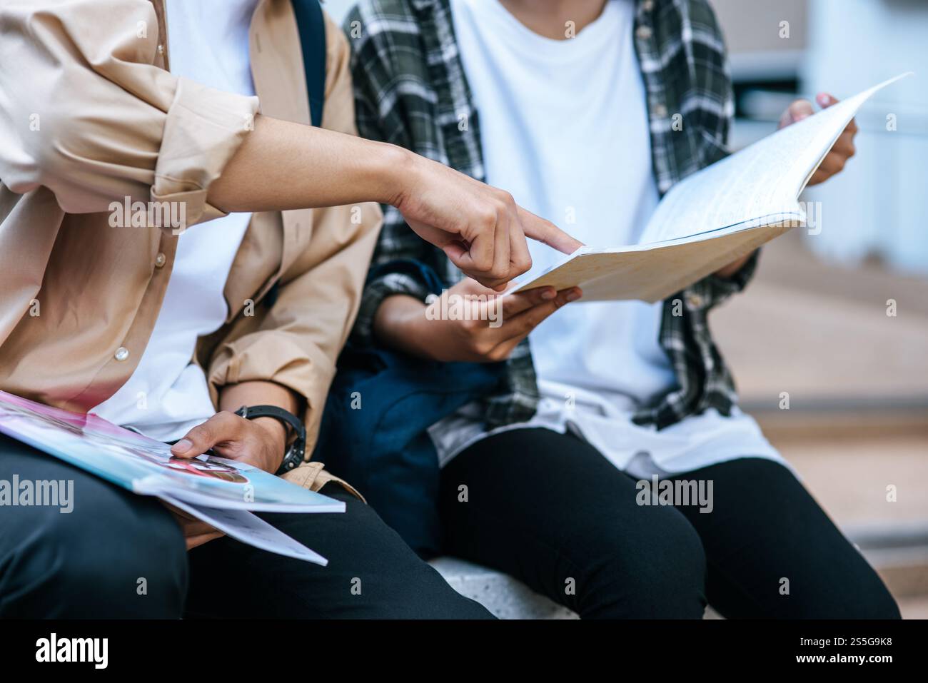 Male and female students wearing masks sit and read books on the stairs ...