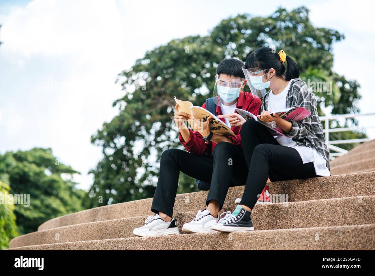 Male and female students wearing masks sit and read books on the stairs ...