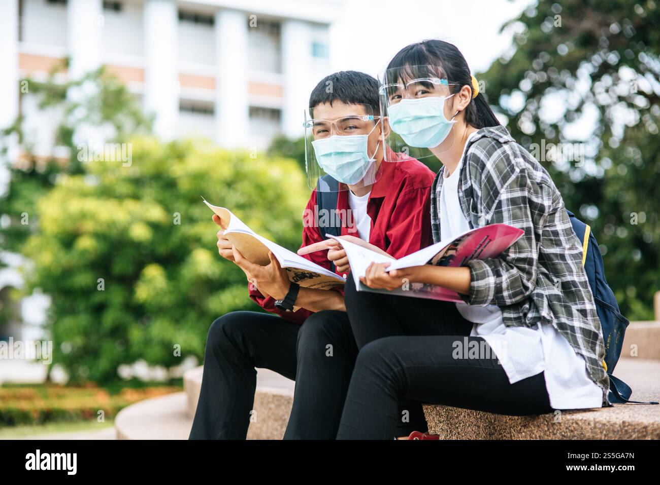 Male and female students wearing masks sit and read books on the stairs ...