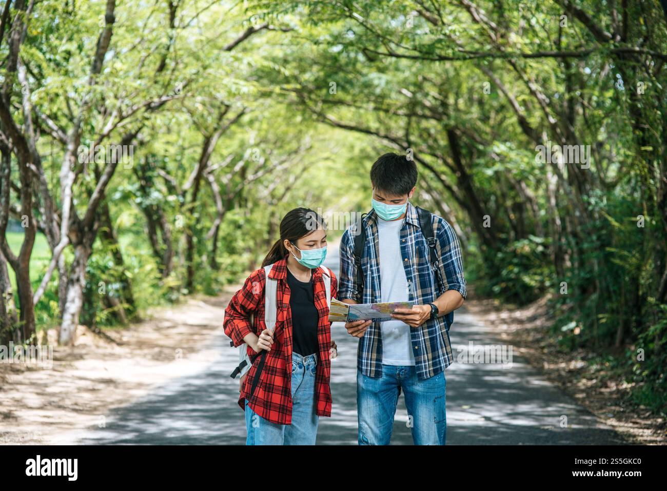 Male and female tourists wear medical masks and look at the map on the ...