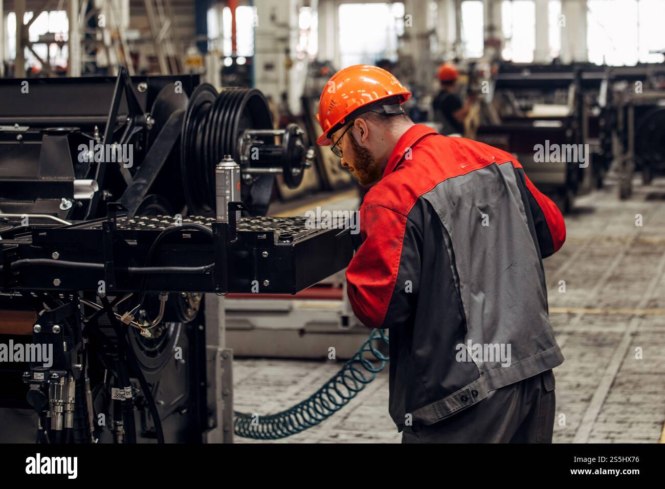 Industrial worker assembles agricultural machine in workshop. Stock Photo