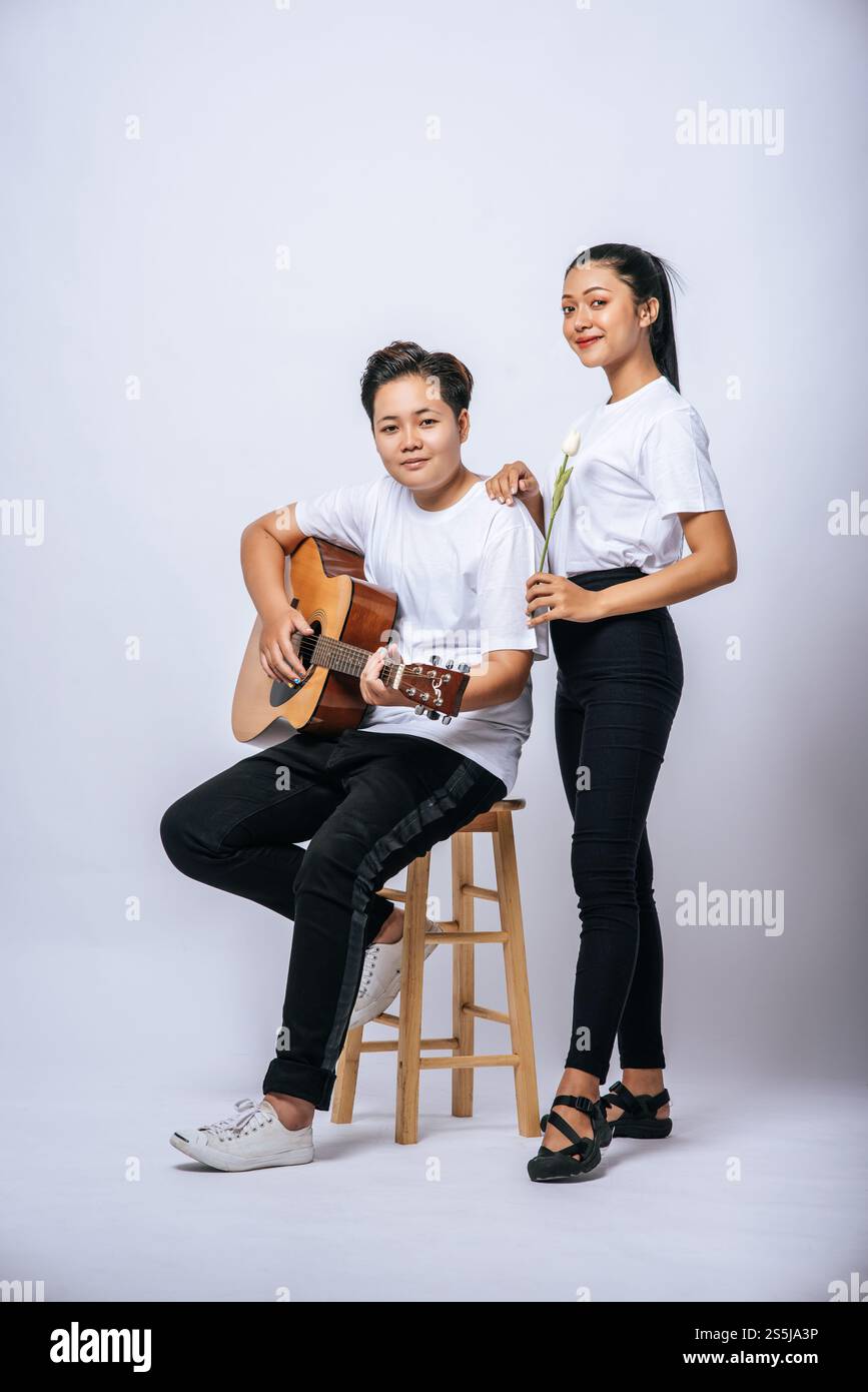 Two young women sat on a chair and played guitar. Stock Photo