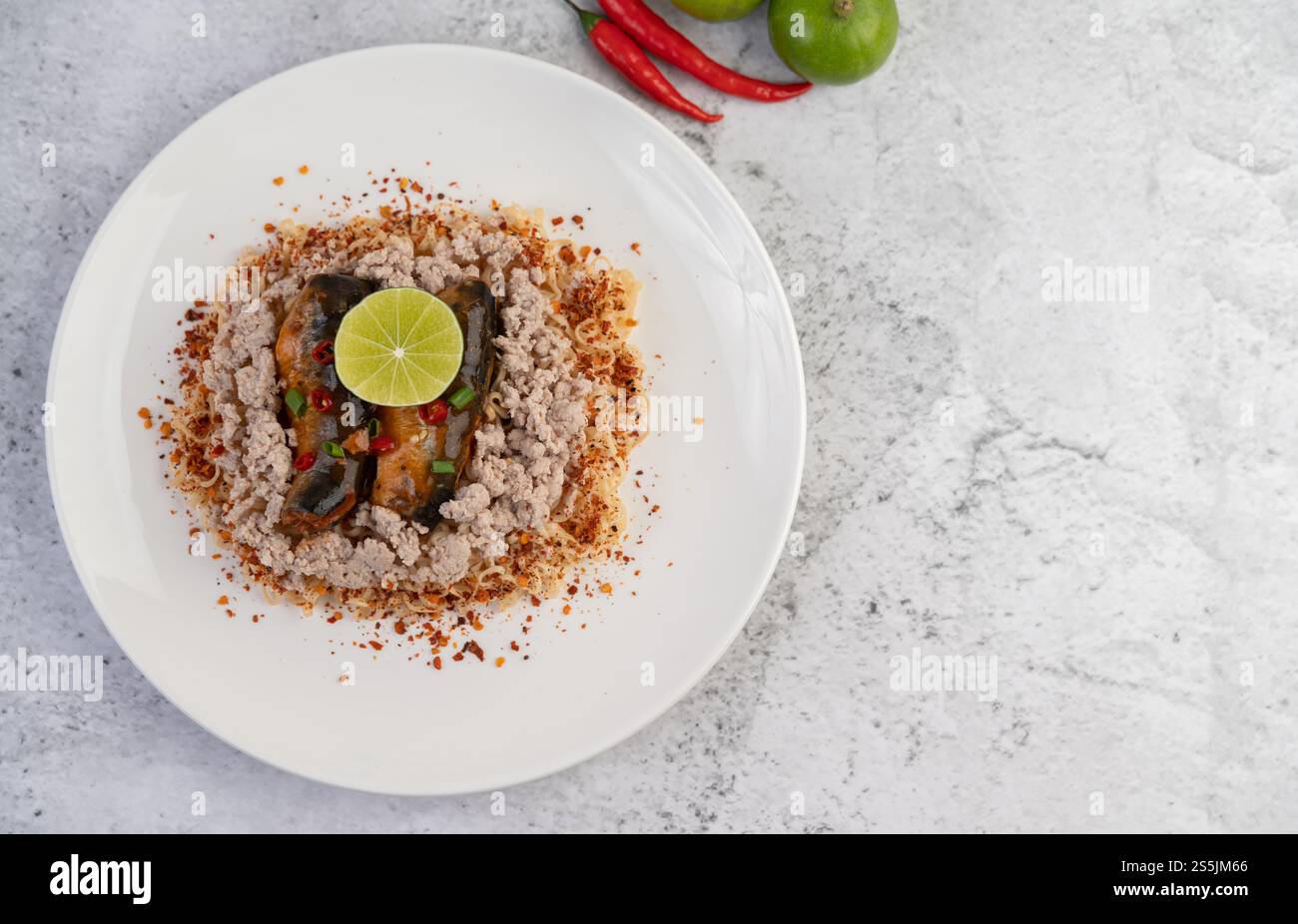 Stir-fried instant noodle with minced pork, canned fish and lemon in a white dish. Stock Photo
