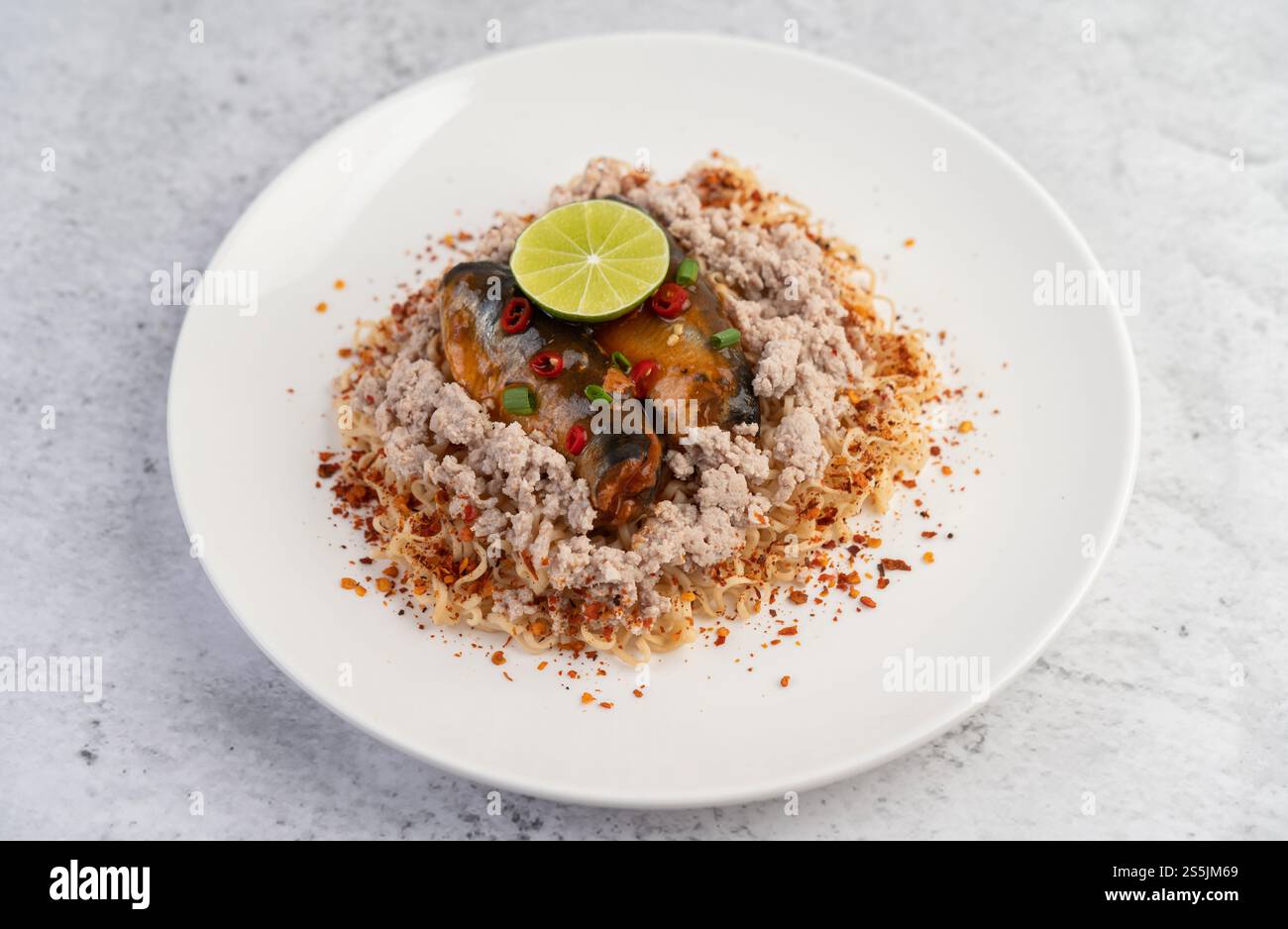 Stir-fried instant noodle with minced pork, canned fish and lemon in a white dish. Stock Photo