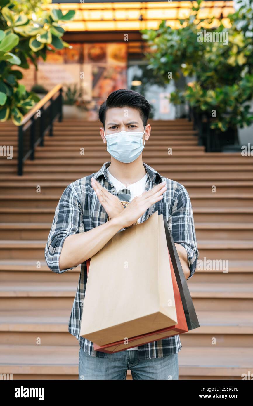 Handsome young man in protection mask holds multiple paper bag and ...