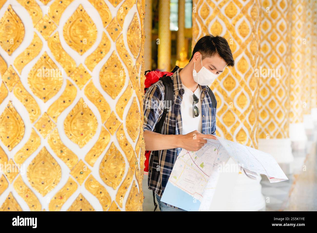 Portrait Young Asian backpacker male in face mask standing and checking ...