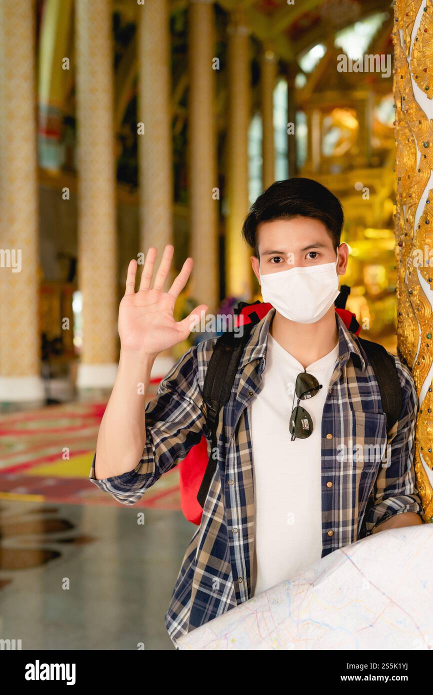 Young Asian backpacker male in face mask standing and checking ...